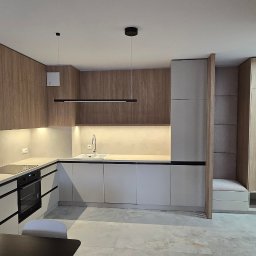 Koral i Kapi Usługi Stolarskie S.C Rafał Koralewski Błażej Błaszczyk - Nowoczesna kuchnia na wymiar z drewnianymi frontami górnych szafek i białymi dolnymi, czarne, minimalistyczne uchwyty, oświetlenie LED pod szafkami, widoczna część jadalni z czarnym stołem...