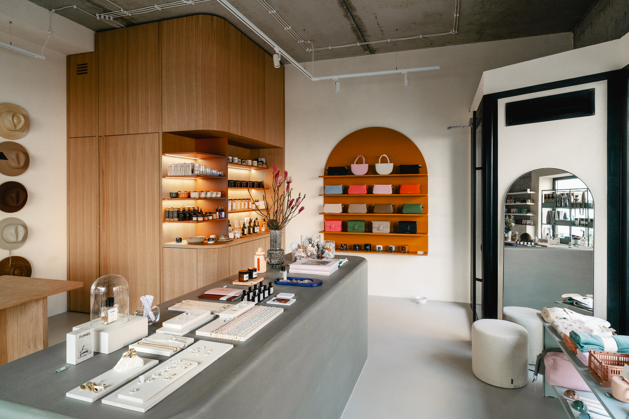 Wnętrze sklepu z drewnianą zabudową, półkami podświetlanymi LED, ekspozycją biżuterii na ladzie i torebkami na pomarańczowych półkach na ścianie.