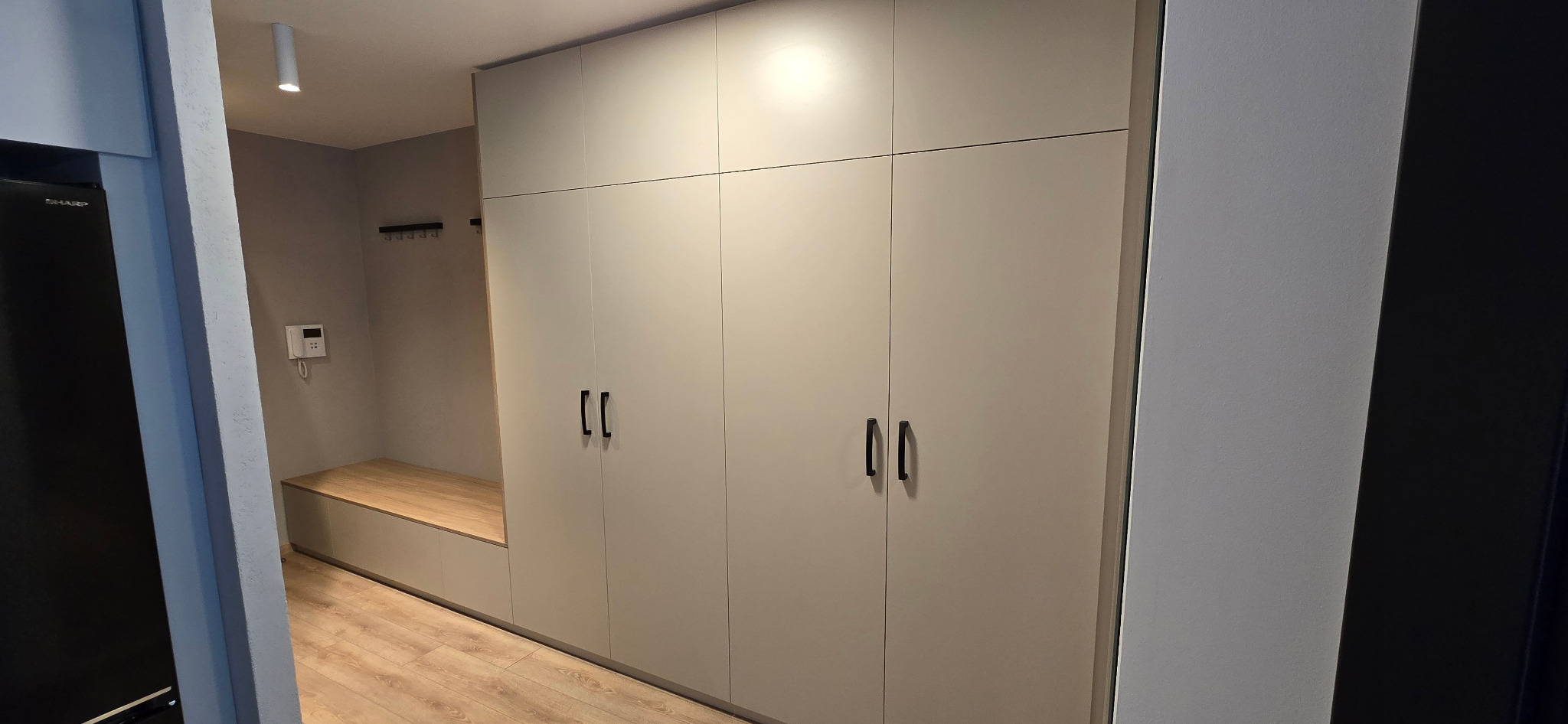 Beżowa szafa na wymiar z czarnymi uchwytami, zintegrowana z siedziskiem z drewnianym blatem w przedpokoju.