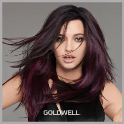 Modelka z ciemnymi włosami z purpurowymi pasemkami, włosy w lekkim ruchu, logo Goldwell na dole zdjęcia.