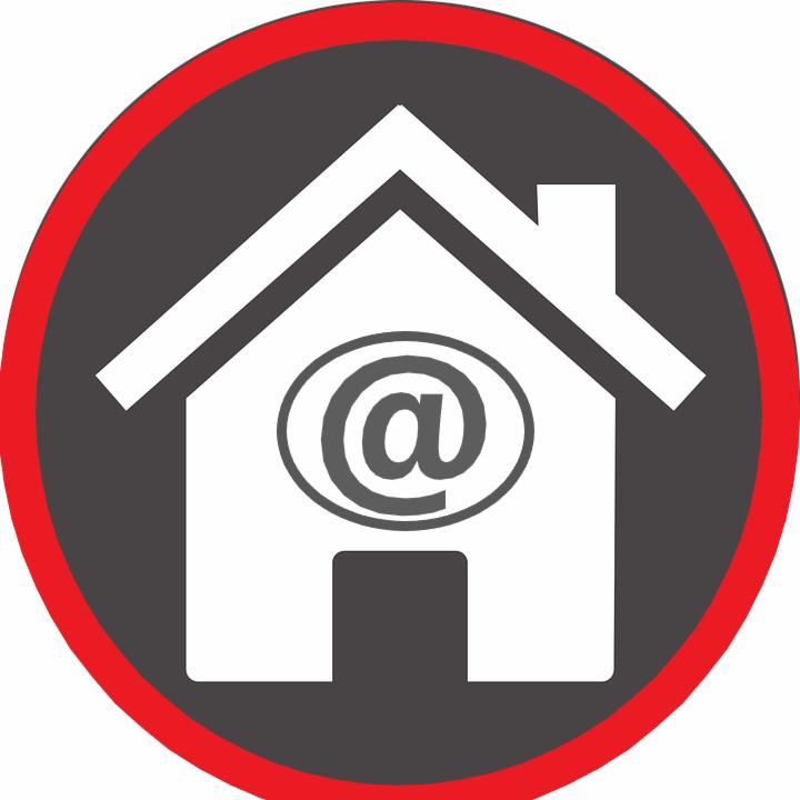 Grafika przedstawia biały kontur domu z symbolem '@' wewnątrz, umieszczony na szarym tle w czerwonym okręgu.