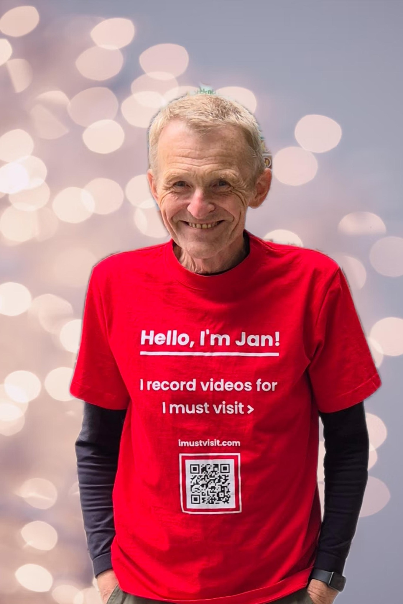 Uśmiechnięty mężczyzna o imieniu Jan w czerwonej koszulce z napisem 'Hello, I'm Jan! I record videos for I must visit >' i kodem QR na tle bokeh.