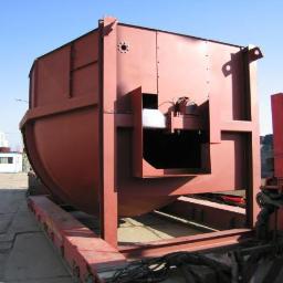 Maguin-Chełmża Sp. z o.o. - Duży, pomalowany na czerwono metalowy zbiornik o skomplikowanej konstrukcji, umieszczony na platformie transportowej. Widoczne elementy spawane i otwory montażowe. W tle budynek przemysłowy z kopułą.