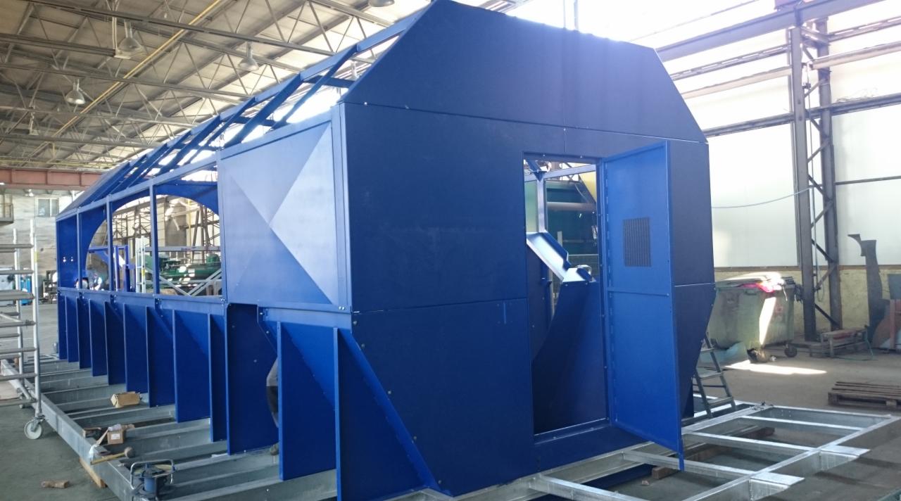 Niebieska, metalowa konstrukcja kabiny na ramie transportowej w hali produkcyjnej, widoczne elementy spawane i skręcane.