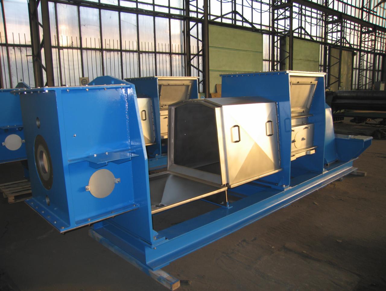 Wykonane z blachy i pomalowane na niebiesko elementy konstrukcyjne, prawdopodobnie obudowy maszyn, ustawione w hali produkcyjnej z widoczną konstrukcją stalową dachu i ścian.