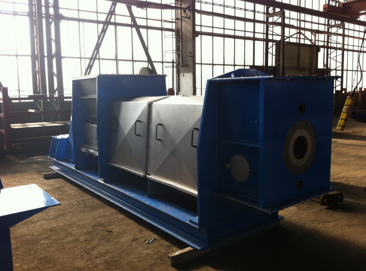 Duże, niebiesko-srebrne urządzenie przemysłowe na metalowej ramie, sfotografowane w hali produkcyjnej z widoczną konstrukcją stalową i oknami w tle.