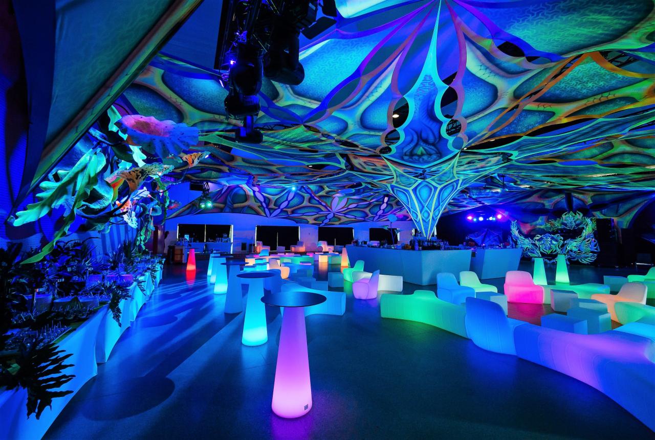 Wnętrze sali bankietowej z futurystycznym wystrojem: podświetlane meble, dekoracje sufitowe w stylu psychedelicznym, rośliny po lewej stronie.