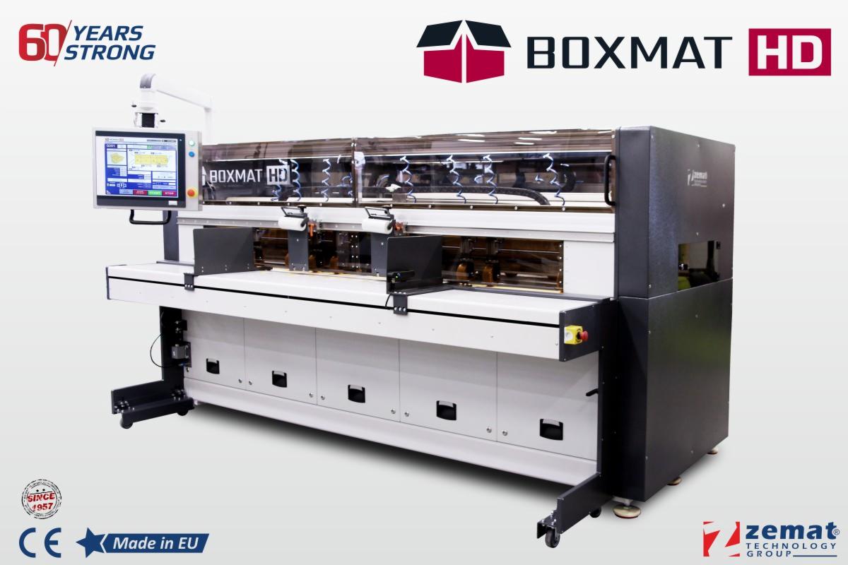 Automatyczna linia produkcyjna BOXMAT HD firmy Zemat, z ekranem sterującym i przezroczystą osłoną, widoczne logo firmy i oznaczenia CE oraz Made in EU.