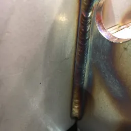 Metalowa konstrukcja z widocznym spoiwem po spawaniu, z charakterystycznymi przebarwieniami termicznymi i otworem w jednym z elementów.