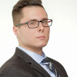 Portret młodego mężczyzny w okularach i garniturze, spoglądającego z powagą w obiektyw na białym tle.