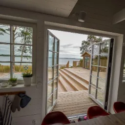 Wnętrze domu z bali z widokiem na taras i jezioro przez otwarte dwuskrzydłowe drzwi balkonowe, dekoracje w stylu marynistycznym.