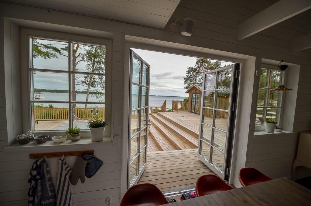 Wnętrze domu z bali z widokiem na taras i jezioro przez otwarte dwuskrzydłowe drzwi balkonowe, dekoracje w stylu marynistycznym.