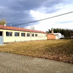 Budynek warsztatu obróbki metali z pomarańczowym dachem i żółtymi ścianami, widok z zewnątrz na tle pochmurnego nieba.