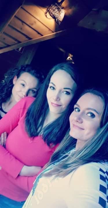 Zdjęcie trzech uśmiechniętych kobiet, zrobione z dołu, z widocznym drewnianym sufitem i lampą w tle. Jedna kobieta w różowej bluzce, druga w bieli z wzorem.