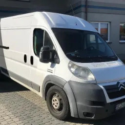 Biały furgon dostawczy marki Citroen z widoczną tablicą rejestracyjną SCZ zaparkowany przed budynkiem o szarym kolorze.