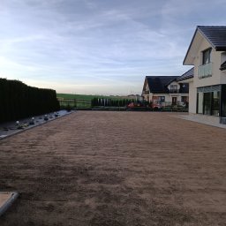 GREEN-BAU TECHNIK Cezary Palęga - Przygotowany teren pod trawnik z rolki, widoczne ślady po wałowaniu. W tle domy jednorodzinne i traktor. Całość w pochmurny dzień.