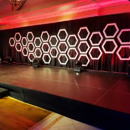 Scena z dekoracją z podświetlanych heksagonów na czarnym tle, oświetlona czerwonym światłem z reflektorów scenicznych i wentylatorem po lewej stronie.