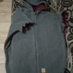 Szary, rozpięty kombinezon dziecięcy z kapturem z uszami i czerwonym wykończeniem, leżący na wzorzystym materiale.