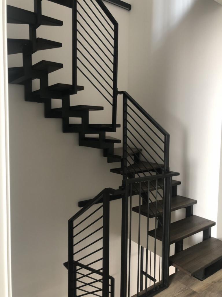 Nowoczesne schody wiszące z metalową balustradą, minimalistyczny design, drewniane stopnie w ciemnym odcieniu, białe ściany.