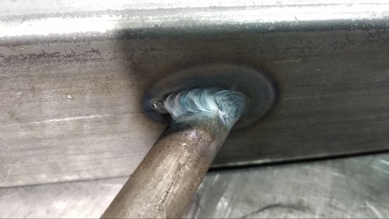 Połączenie spawane rury z grubą blachą, widoczne ślady po spawaniu i przebarwienia termiczne na metalu.