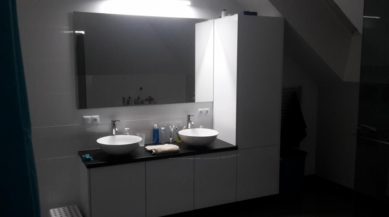 Nowoczesna łazienka z dwoma białymi umywalkami nablatowymi, czarnym blatem i dużym lustrem na tle skośnego sufitu poddasza.