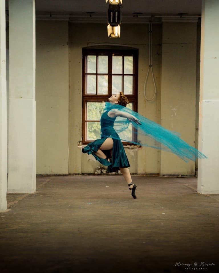 Baletnica w zielonej sukience i turkusowym tiulu w skoku na tle okna w opuszczonym budynku.