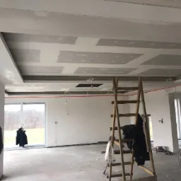 Montaż płyt kartonowo-gipsowych na suficie w Zielonej Górze, widoczny drewniany drabina, surowe wnętrze w trakcie prac wykończeniowych.
