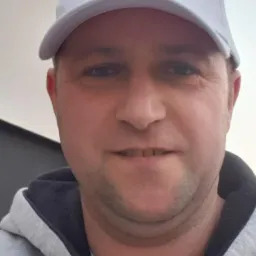 Portret mężczyzny w czapce z logo Graco, prawdopodobnie pracownika firmy remontowej, na tle ściany.