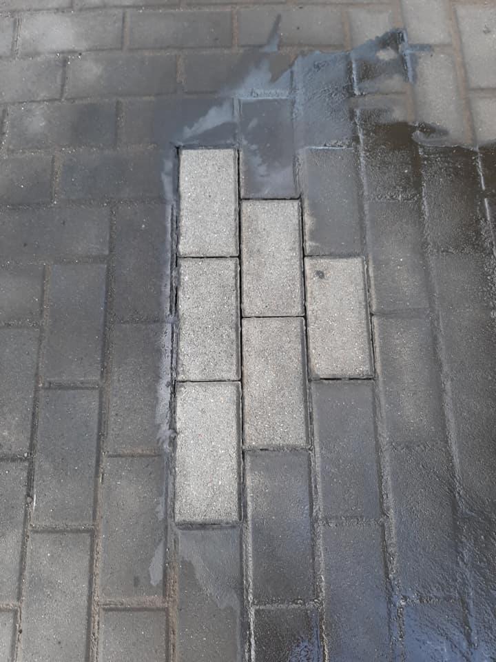 Fragment powierzchni z kostki brukowej, gdzie część kostek jest wyraźnie jaśniejsza i sucha, a pozostała część jest ciemniejsza i mokra, sugerując proces czyszczenia lub mycia pod ciśnieniem.