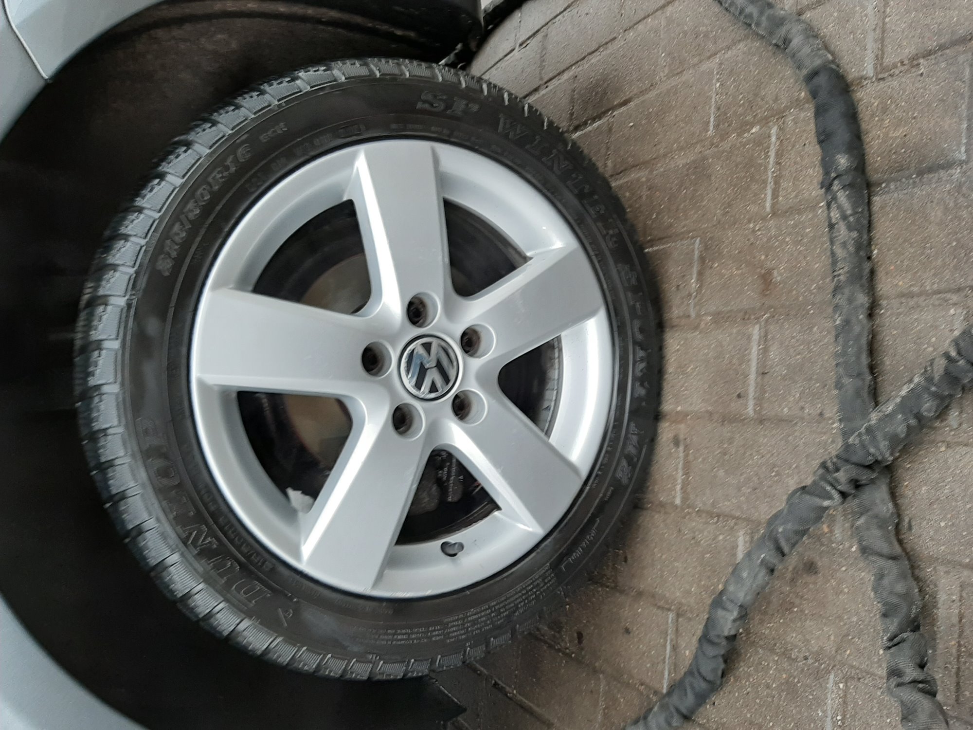 Koło samochodowe z aluminiową felgą Volkswagen na tle ściany z cegieł i grubego węża ciśnieniowego.