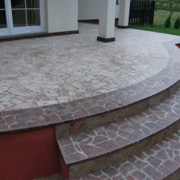 Zewnętrzne schody z granitu prowadzące do tarasu z nieregularnych płyt kamiennych, widok z bliska na zaokrąglone stopnie.