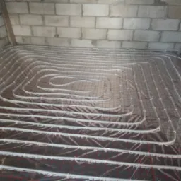 Rozłożona instalacja ogrzewania podłogowego na folii izolacyjnej z siatką, widok na surowe ściany z białego pustaka.