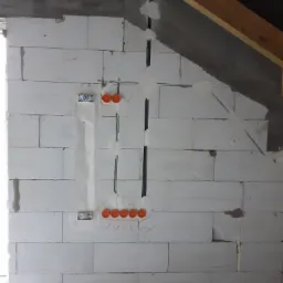 Ściana z betonu komórkowego w trakcie prac elektrycznych: widoczne bruzdy z przewodami, puszki instalacyjne zalane gipsem, oznaczenia ołówkiem. Poddasze w stanie surowym.