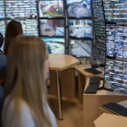 Centrum monitoringu wizyjnego z wieloma ekranami wyświetlającymi obraz z kamer CCTV, w tle siedzą dwie osoby.