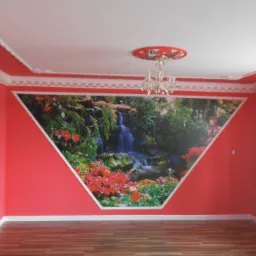 Pokój z czerwonymi ścianami, dekoracyjnymi listwami sufitowymi i trójkątnym fototapetą przedstawiającą wodospad i roślinność.