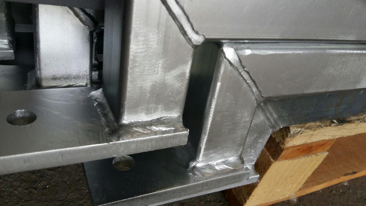 Szczegółowe ujęcie spawanych, metalowych elementów konstrukcyjnych, ukazujące spoiny i obróbkę powierzchni. Widoczne ślady szlifowania i spawania na błyszczącej powierzchni metalu.