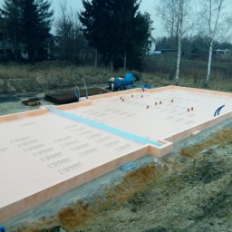 Bodnenplatte Sp. z o.o. - Przygotowany fundament z izolacją termiczną, widoczne wystające rurki instalacyjne, teren budowy z drzewami w tle.