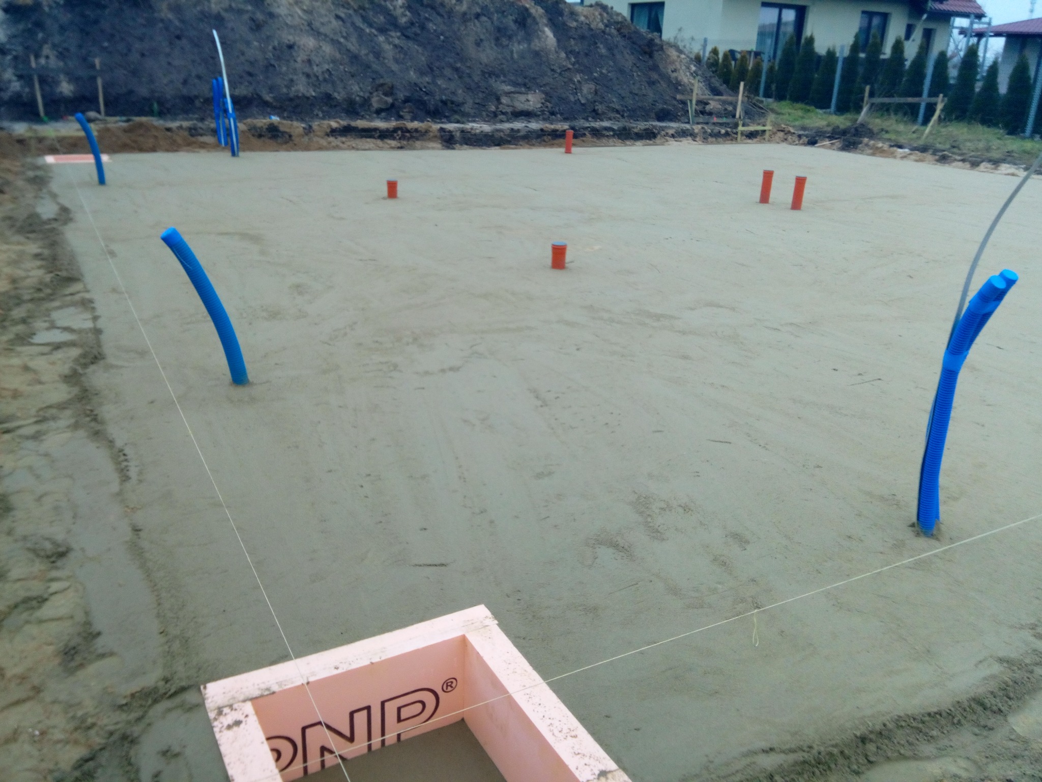 Przygotowany teren pod wylanie fundamentów z wystającymi rurami instalacyjnymi, obrzeżem z różowego styropianu i wytyczonymi sznurami.