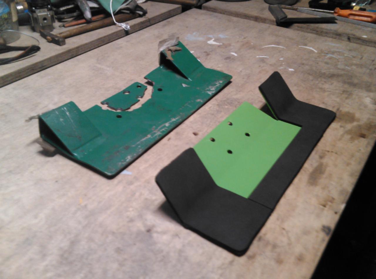 Porównanie starego, uszkodzonego elementu metalowego w kolorze zielonym z nowym, odnowionym elementem z czarną ramą i zielonym środkiem na warsztatowym stole.