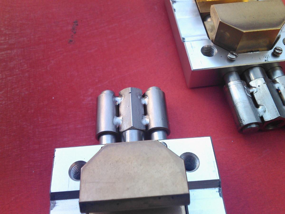 Metalowa konstrukcja z elementami połączonymi spawami, widoczne ślady obróbki skrawaniem, ułożona na czerwonym tle.