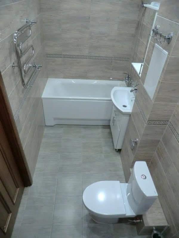 Jasna łazienka z beżowymi płytkami, widok z góry na wannę, umywalkę z szafką, toaletę i grzejnik drabinkowy.