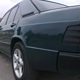 Ciemnozielony samochód osobowy, widok z boku, zarys drzew odbity w lakierze, felgi aluminiowe