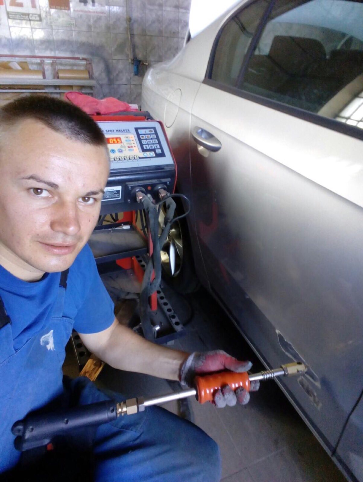 Pracownik warsztatu samochodowego, z bliska, w trakcie usuwania wgniecenia na srebrnym samochodzie za pomocą specjalistycznego urządzenia do wyciągania wgnieceń, z widocznym panelem sterowania...