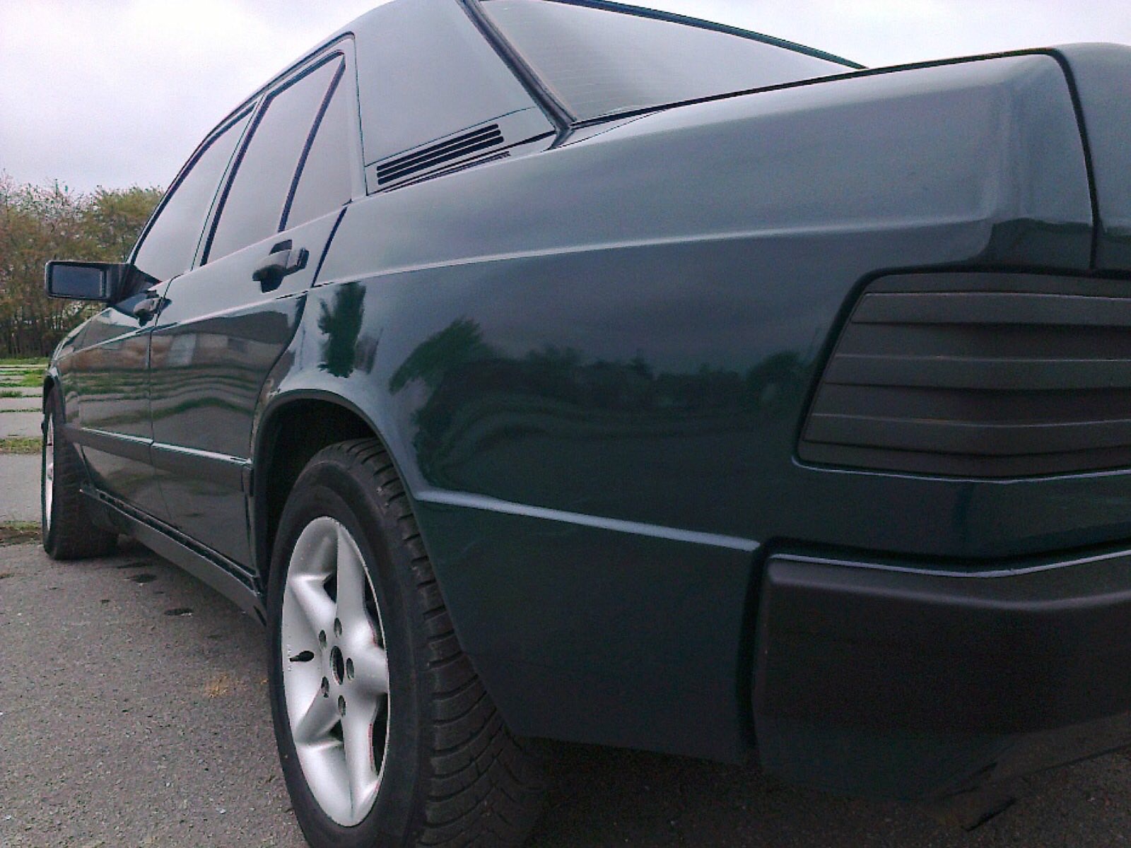 Ciemnozielony samochód osobowy, widok z boku, zarys drzew odbity w lakierze, felgi aluminiowe