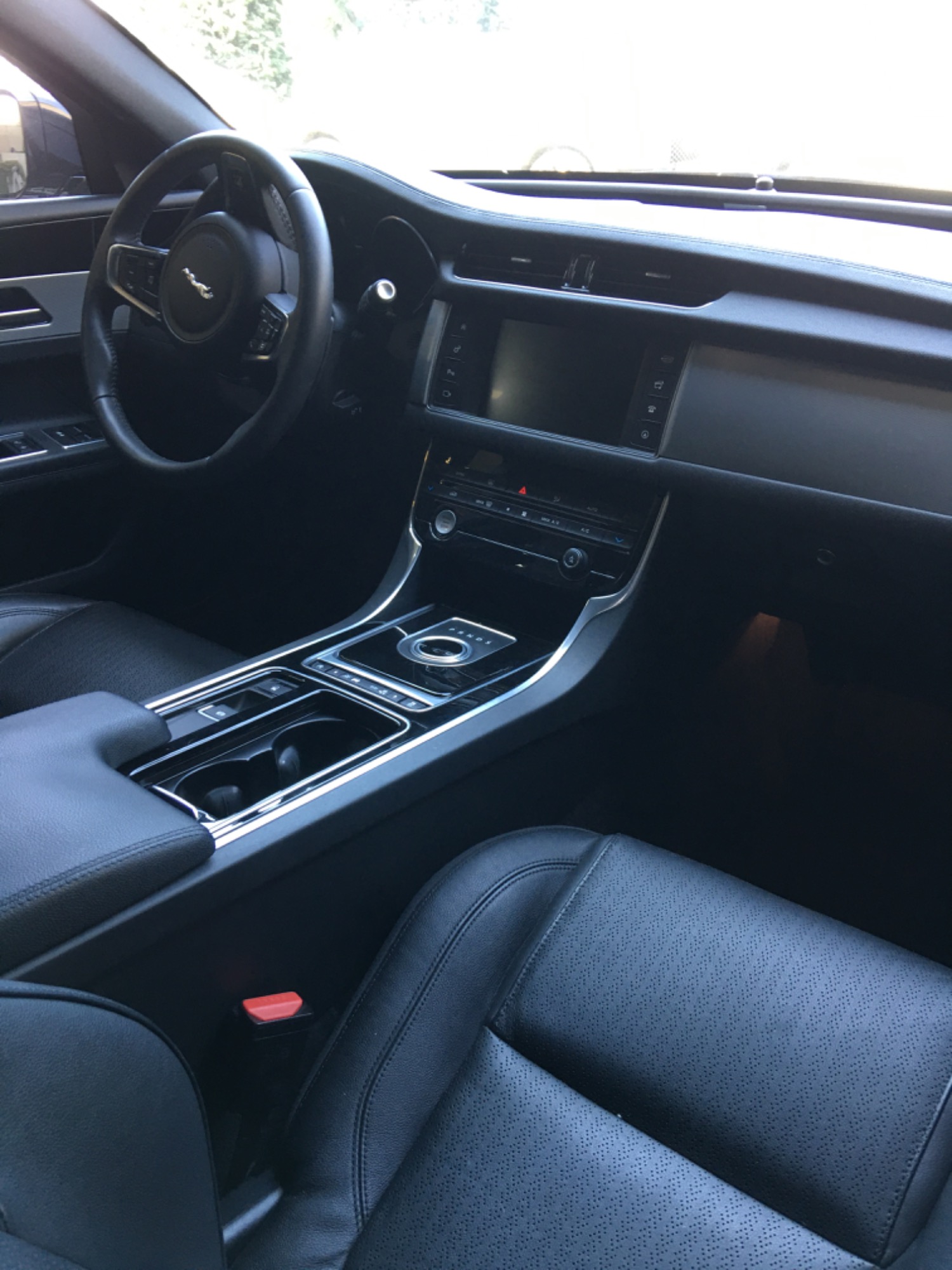 Wnętrze samochodu Jaguar z czarną skórzaną tapicerką, widoczna deska rozdzielcza, kierownica z logo, konsola środkowa z chromowanymi elementami i cup holderami.