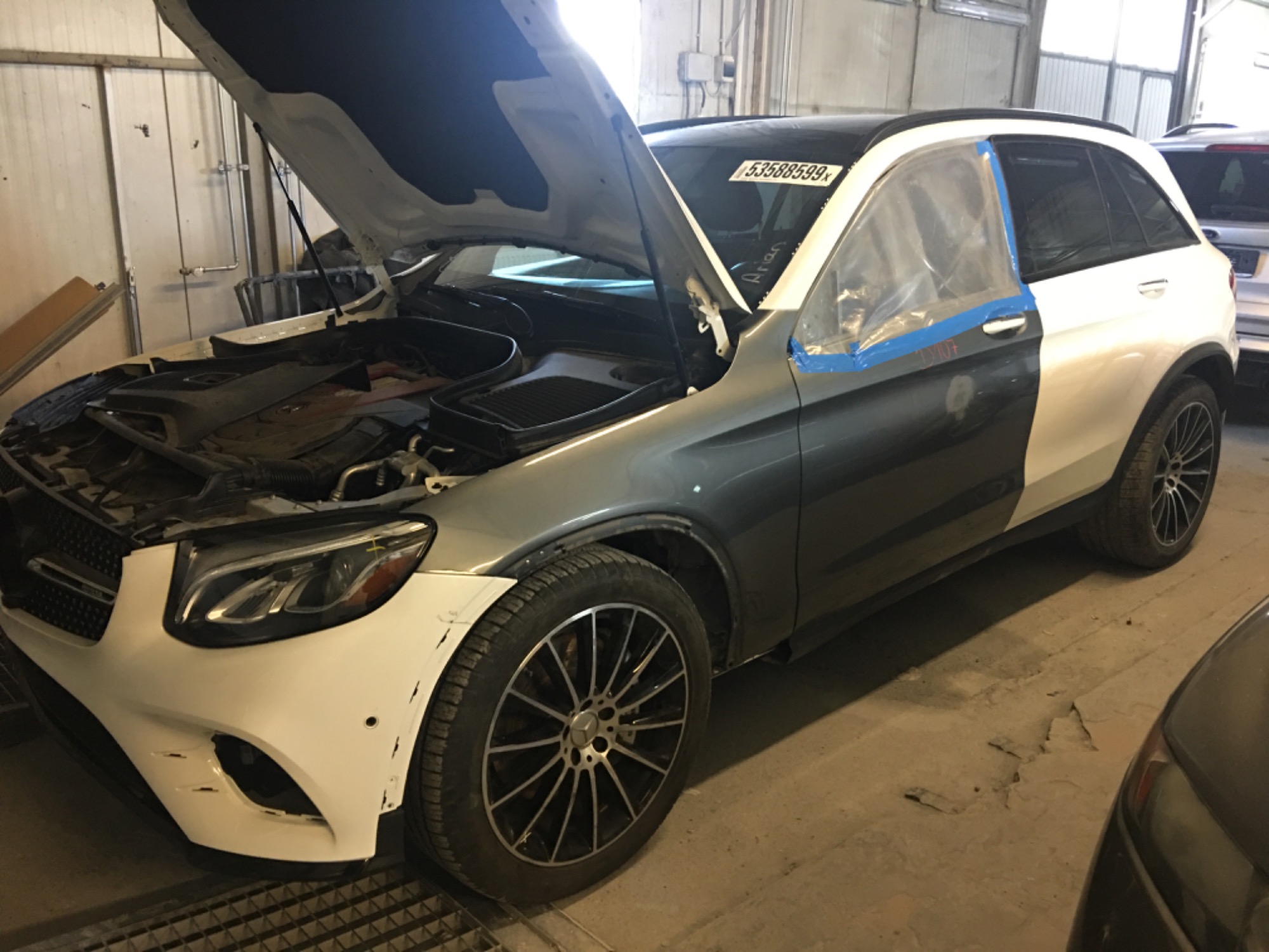 Mercedes GLC w trakcie naprawy blacharsko-lakierniczej, z otwartą maską i zabezpieczoną folią szybą, widoczne uszkodzenia na zderzaku.