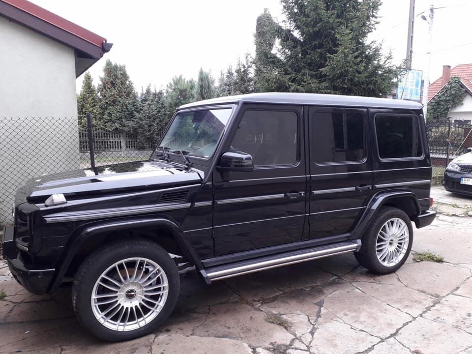 Błyszczący, czarny Mercedes-Benz klasy G z aluminiowymi felgami zaparkowany na betonowym podjeździe przed domem.