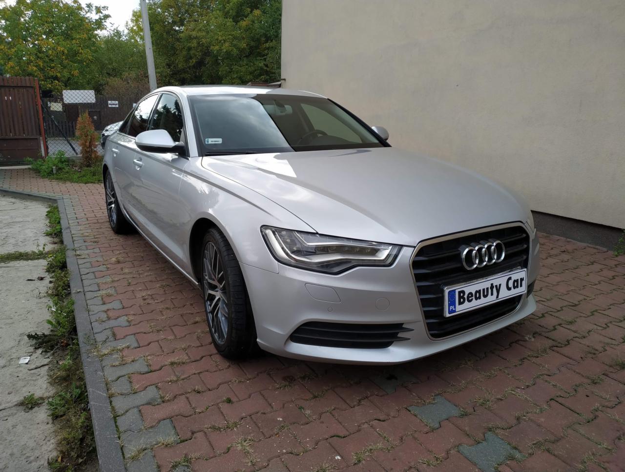 Srebrny sedan Audi A6 po umyciu, zaparkowany na kostce brukowej przed budynkiem, z widoczną tablicą rejestracyjną z napisem 'Beauty Car'.