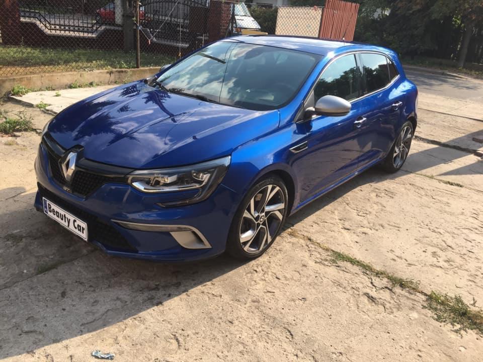 Błyszczący, granatowy Renault Megane po myciu, zaparkowany na betonowym podjeździe w słoneczny dzień, z widoczną tabliczką 'Beauty Car' na przednim zderzaku.