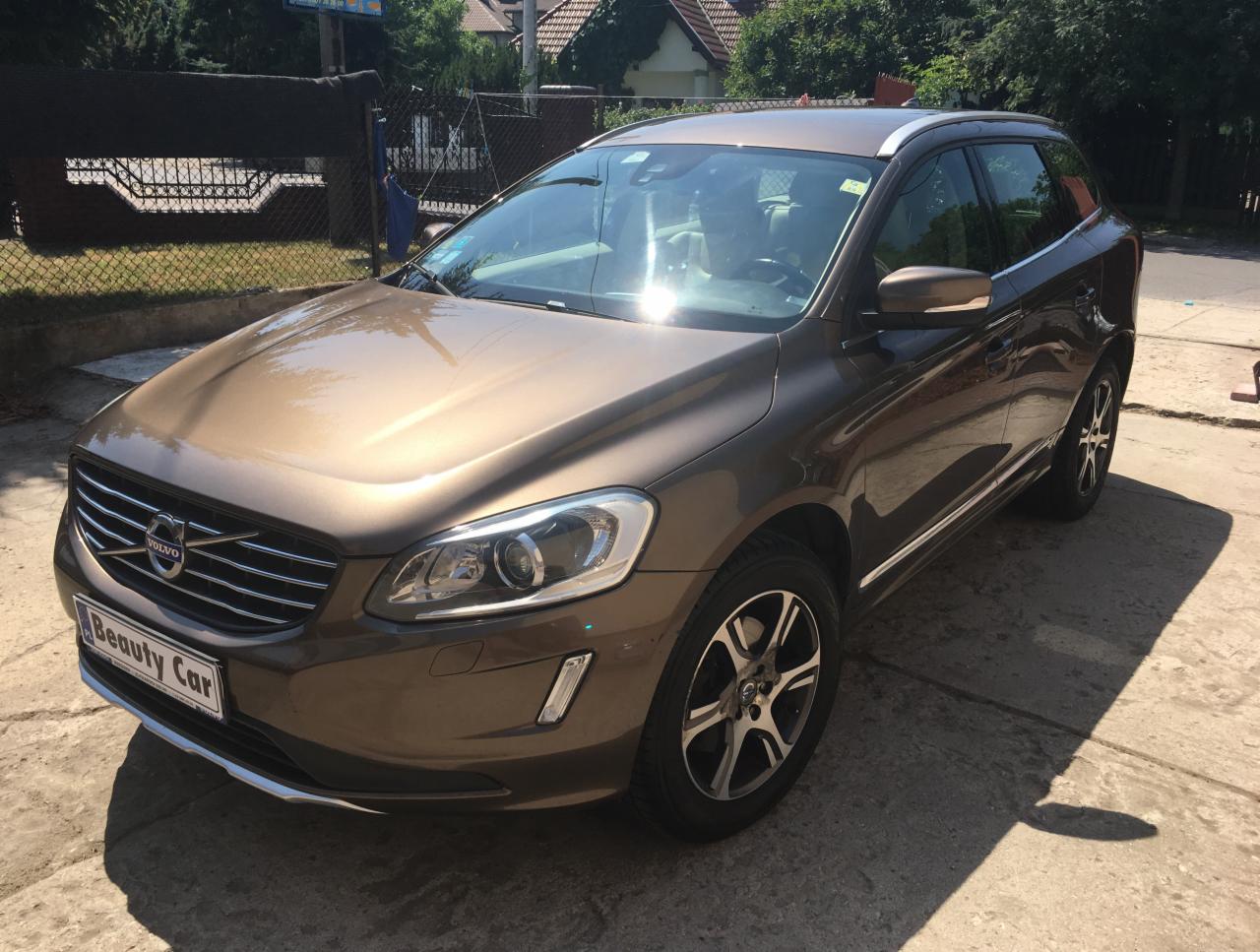 Brązowy samochód Volvo XC60 zaparkowany na betonowej nawierzchni w słoneczny dzień, widoczny napis 'Beauty Car' na tablicy rejestracyjnej.